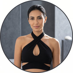 Portrait of Amina El-Sayed wearing a black halter cutout crop top against a minimalist charcoal and slate gray background.