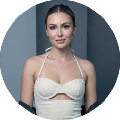 A circular portrait of Tess Thorne wearing a stylish halter cutout crop top against a minimalist slate gray studio background